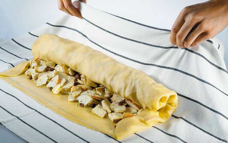 Une fois que la pâte est étirée finement, le strudel est enroulé à l’aide d’un linge ou d’un papier cuisson.